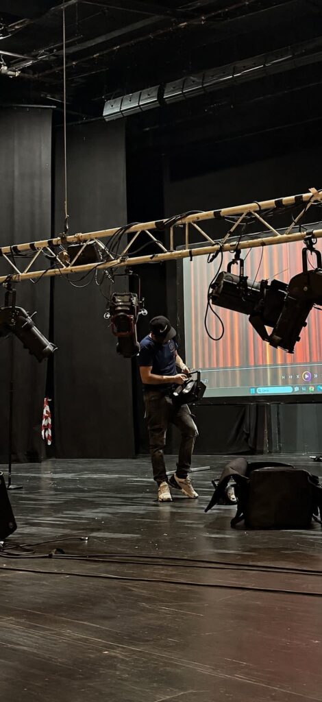 Techniker bestückt eine abgelassene Traverse mit Scheinwerfern auf einer Theaterbühne