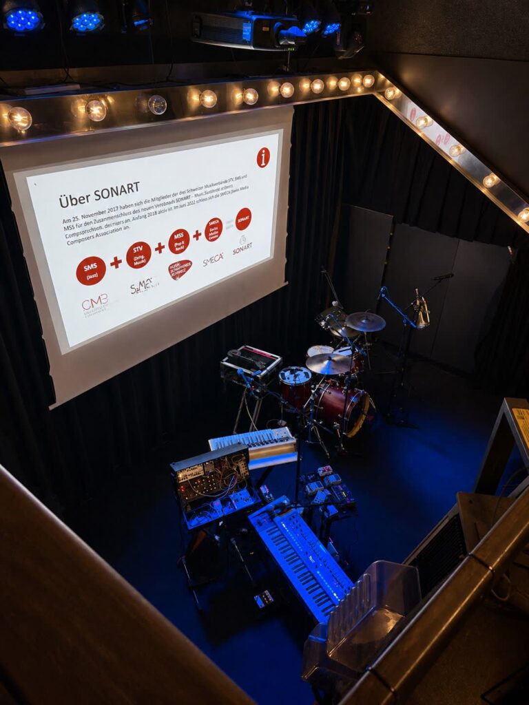 Projektion auf Leinwand mit Beamer an der Traverse über einer Bühne mit Instrumenten
